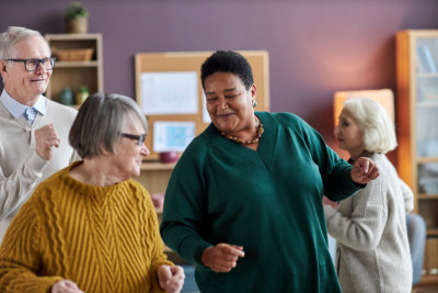 elder woman dancing with friends in retirement home and smiling joyfully