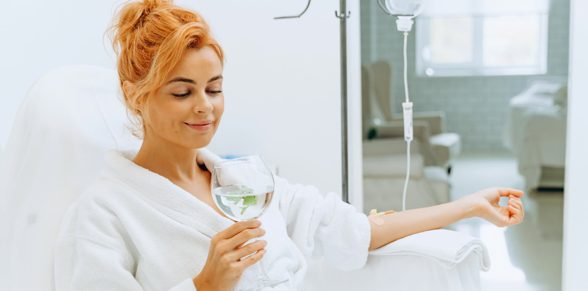 a woman drinking a glass of water while doing a iv hydration