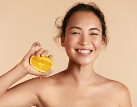 Woman with radiant face skin squeezing orange in hand portrait.