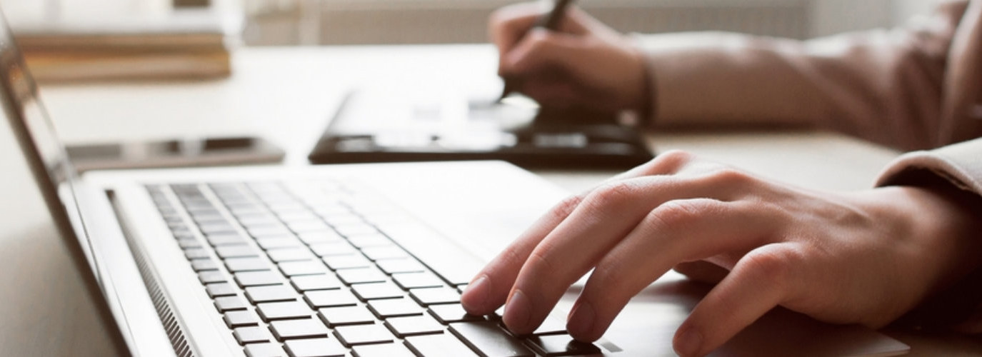 person using laptop while writing on other hand