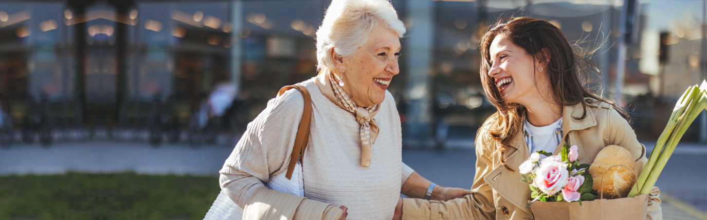 A joyful elderly woman and a young woman sharing a happy moment after shopping.