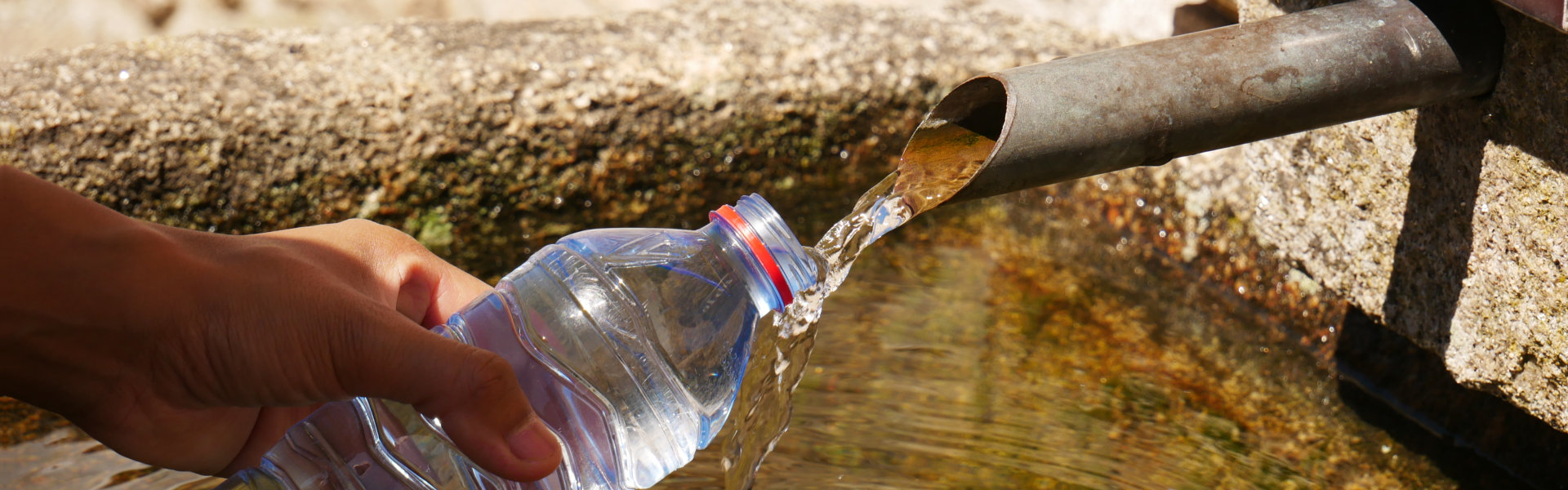 A closeup shot of a hand holding a plastic bottle and filling with drinking water