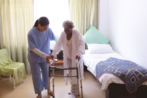 Front view of mixed race female nurse helping senior mixed race female patient to stand with walker at nursing home