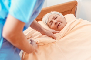 Caregiver pulling blanket over sleeping senior in pensioners home for better sleep